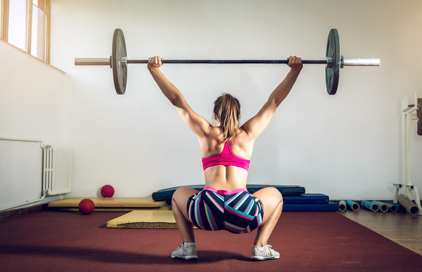 Young adult girl doing heavy duty  squats in gym with barbell